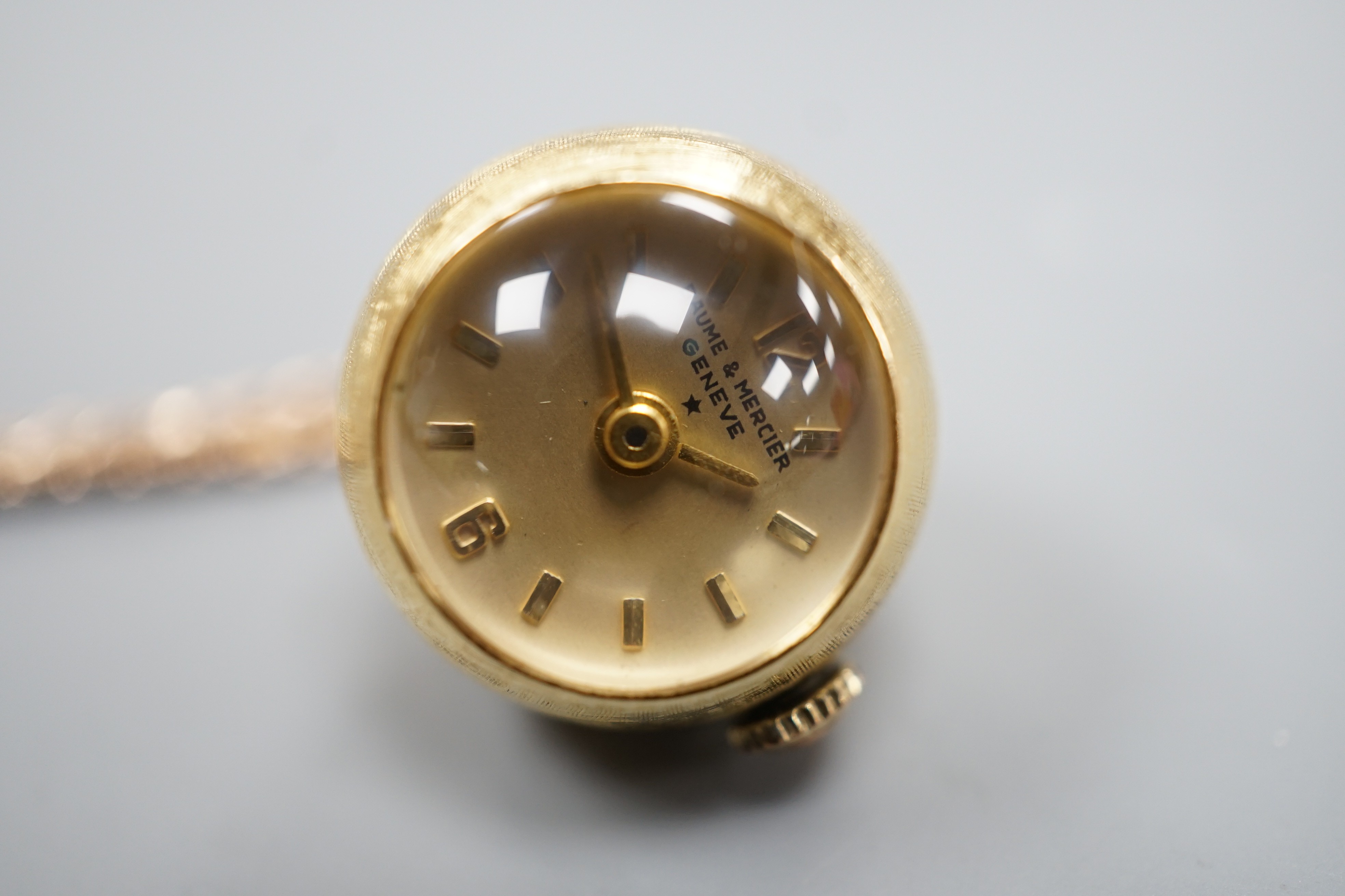 A modern 750 yellow metal Baume & Mercier globe pendant watch, diameter approx. 18mm, on an associated 9ct gold chain, 68cm, chain 6.4 grams.